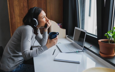 Frau im Homeoffice blickt traurig zum Fenster