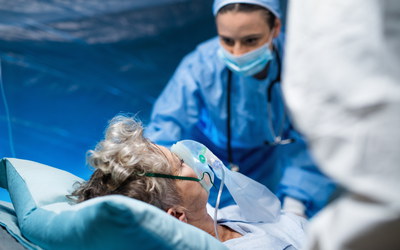 Ältere Corona-Patientin im Krankenzimmer mit Atemmaske, Krankenschwester daneben