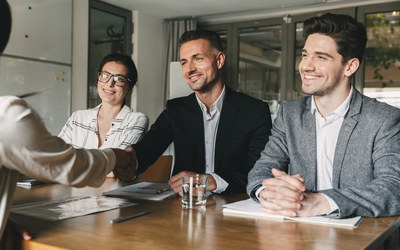 Drei Firmenvertreter und Bewerberin, einer gibt ihr die Hand (Jobzusage)