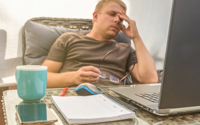 Mann sitzt erschöpft im Homeoffice vor seinem Laptop