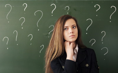 Junge Frau vor Tafel mit Fragezeichen