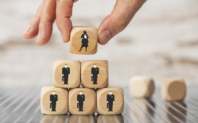 männliche Hand stellt Scrabble-Stein mit Frauenfigur an Spitze einer Pyramide