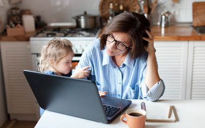 Frau arbeitet am Laptop am Küchentisch und wird von ihrer Tochter gestört