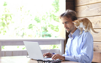 Mann im Homeoffice am Laptop mit Katze auf Schulter