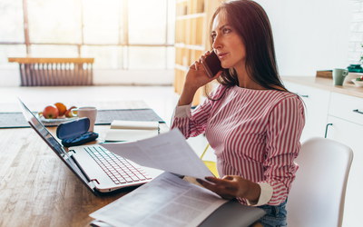 Frau in Homeoffice am Esstisch mit Laptop telefoniert