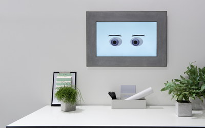 Homeoffice-Arbeitsplatz, an der Wand Monitor mit Augen
