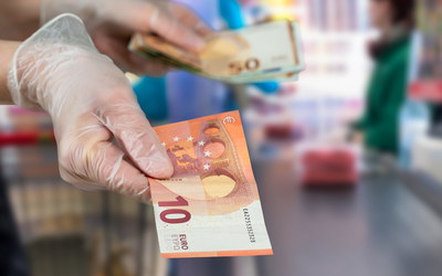 Supermarkt, an Kasse Kunde mit Einmalhandschuhen, bezahlt mit Bargeld