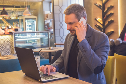 Mann in Business-Kleidung arbeitet im Café am Laptop und telefoniert mit dem Handy
