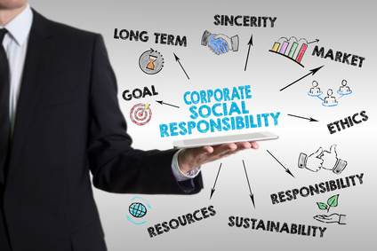 Die Hand eines Mannes in Businesskleidung hält ein Tablet in der Hand, über dem Corporate Social Responsibility steht und das kreisförmig von Einzelaspekten - durch Linien verbunden - umgeben.