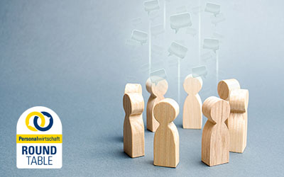 Holzfiguren stehen im Kreis; über ihnen schweben Sprechblasen.