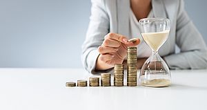 Frau stapelt Münzen neben Sanduhr.