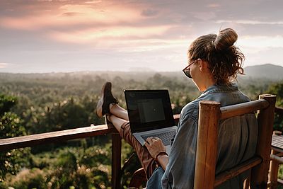 Frau sitzt mit Laptop auf Veranda.