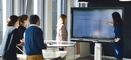 Mehrere Personen stehen vor einem Whiteboard und bekommen etwas gezeigt.