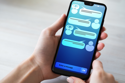 Hand hält Smartphone, dort Chatbot-Unterhaltung