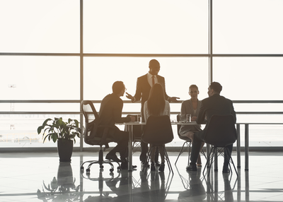 Business-Leute - eine Frau, meherere Männer, in einem edlen Gebäude mti großer Fensterfront arbeiten um einen Tisch herum