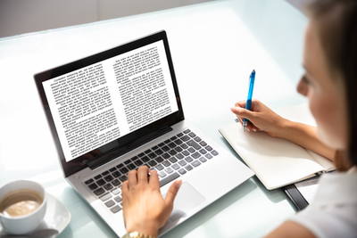 Frau liest auf Laptop Text und macht Notizen auf einem Block