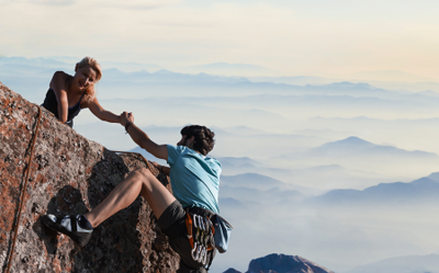 Ein Mann und eine Frau klettern auf einen Berg die Frau reicht dem Mann helfend die Hand. 