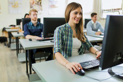 Unterrichtsraum mit jungen Leuten, die Computerunterricht haben, im Vordergrund eine motiviert aussehende junge Frau