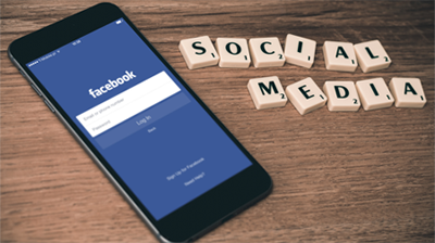 Smartphone mit Facebook-Seite und daneben Skrabble-Steine