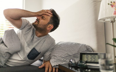 Mann morgens im Bett mit Kopfschmerzen