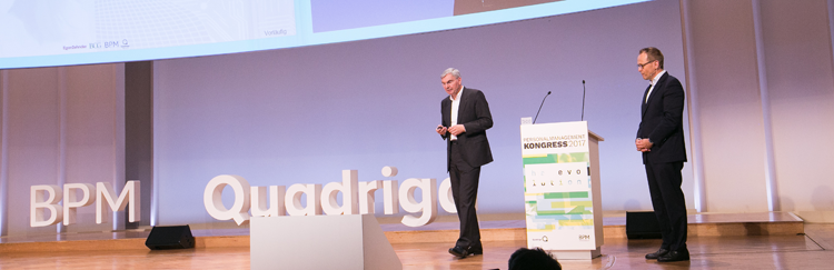 Prof. Dr. Jörg Ritter, Quadriga Hochschule, und Prof. Dr. Rainer Strack stehen zusammen auf der Bühne des BPM
