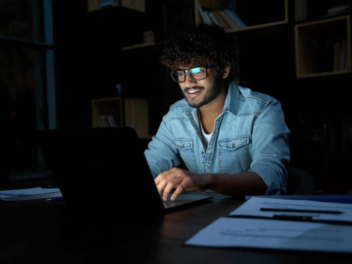 Ein Mitarbeiter, der tief in der Nacht noch hochmotiviert und mit einem Lächeln auf den Lippen weiterarbeitet: Das gibt es auf Stock-Bildern möglicherweise häufiger als in der Realität. (Foto: insta_photos - stock.adobe.com)